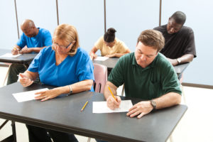 Classrom of adult education students taking a test in school . Focus on the guy in the front.